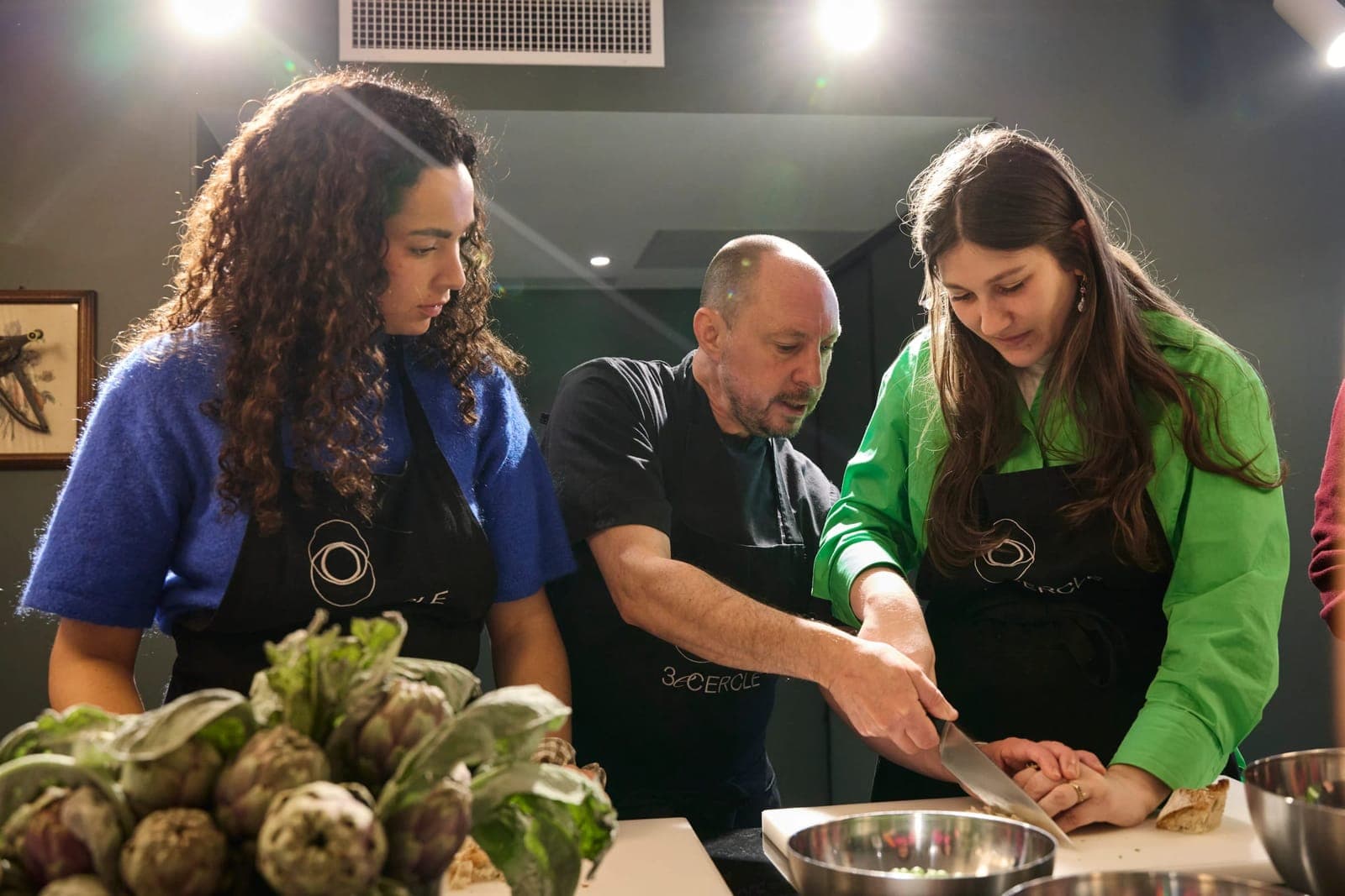 The chef guiding two students at the worktop, Signature cooking class, Paris 11